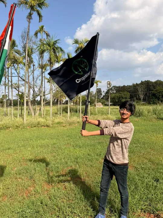 A young man holding up a CropNow flag in a grassy field
